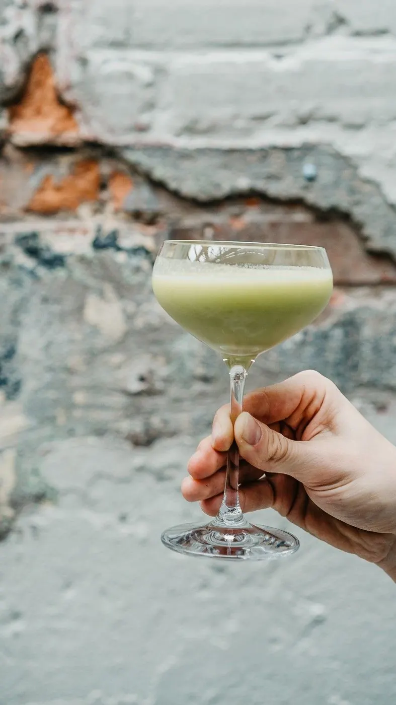 A hand holding a cocktail against a brick wall